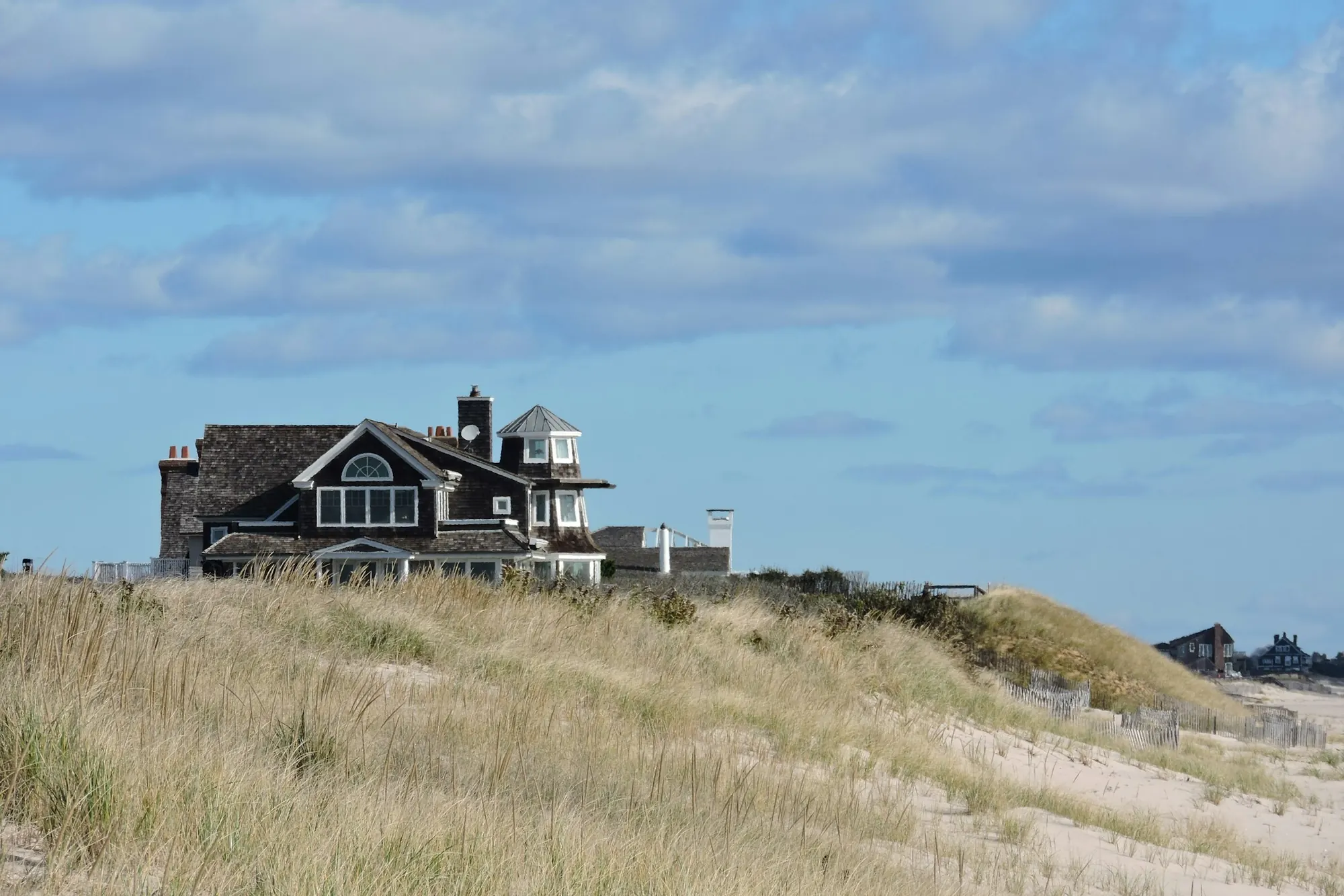 Shingle-style house on a grassy dune under a wide summer sky