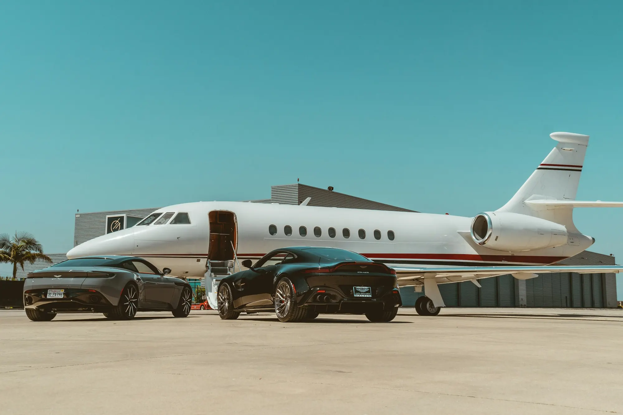 Business jet on a sunny ramp with two dark sports cars parked beside it